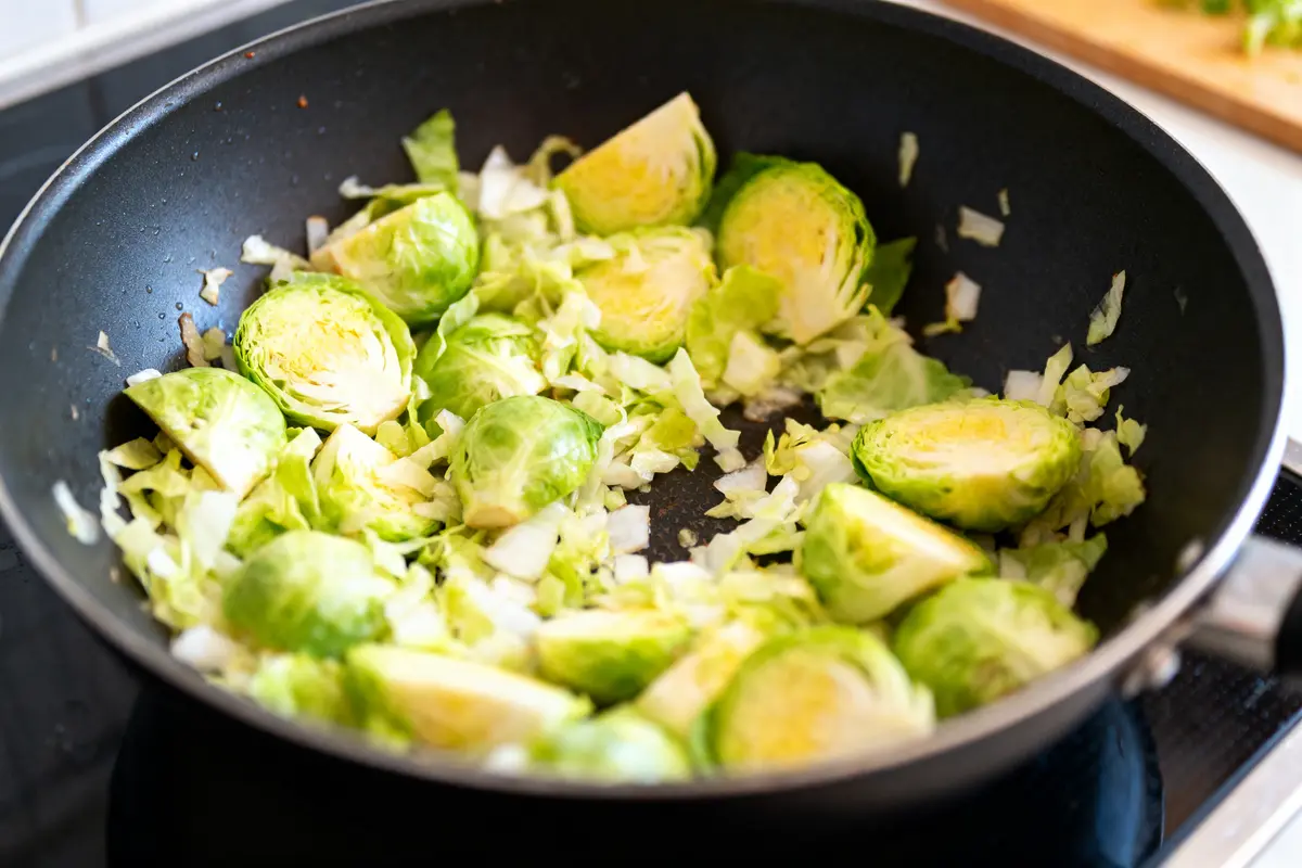 Choux de Bruxelles coupés cuits dans une poêle noire avec des morceaux d'oignon.