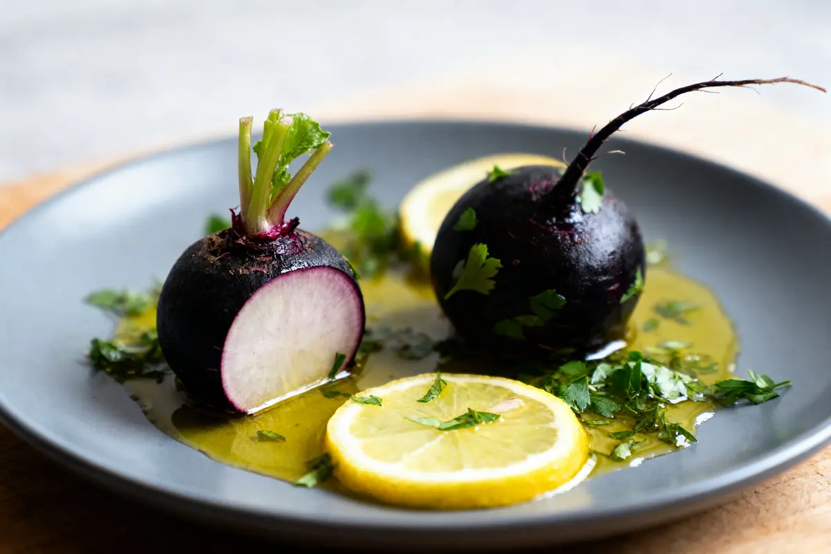 Deux radis noirs, tranches de citron, coriandre, vinaigrette sur assiette grise, vue rapprochée.