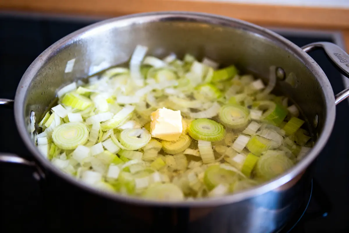 Tranches de poireaux et beurre fondant dans une casserole remplie d'eau sur une cuisinière.
