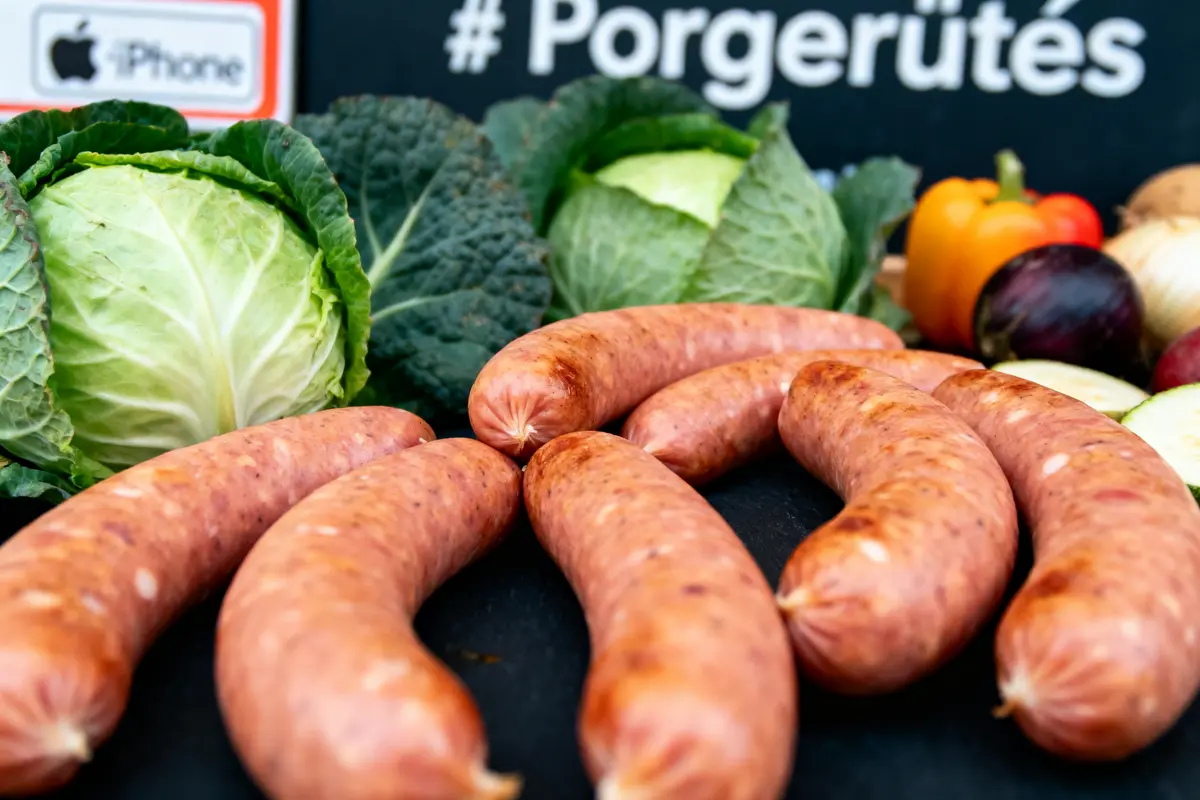 Saucisses sur une table avec choux, poivron, oignons et courgettes, étiquette "iPhone" en arrière-plan.